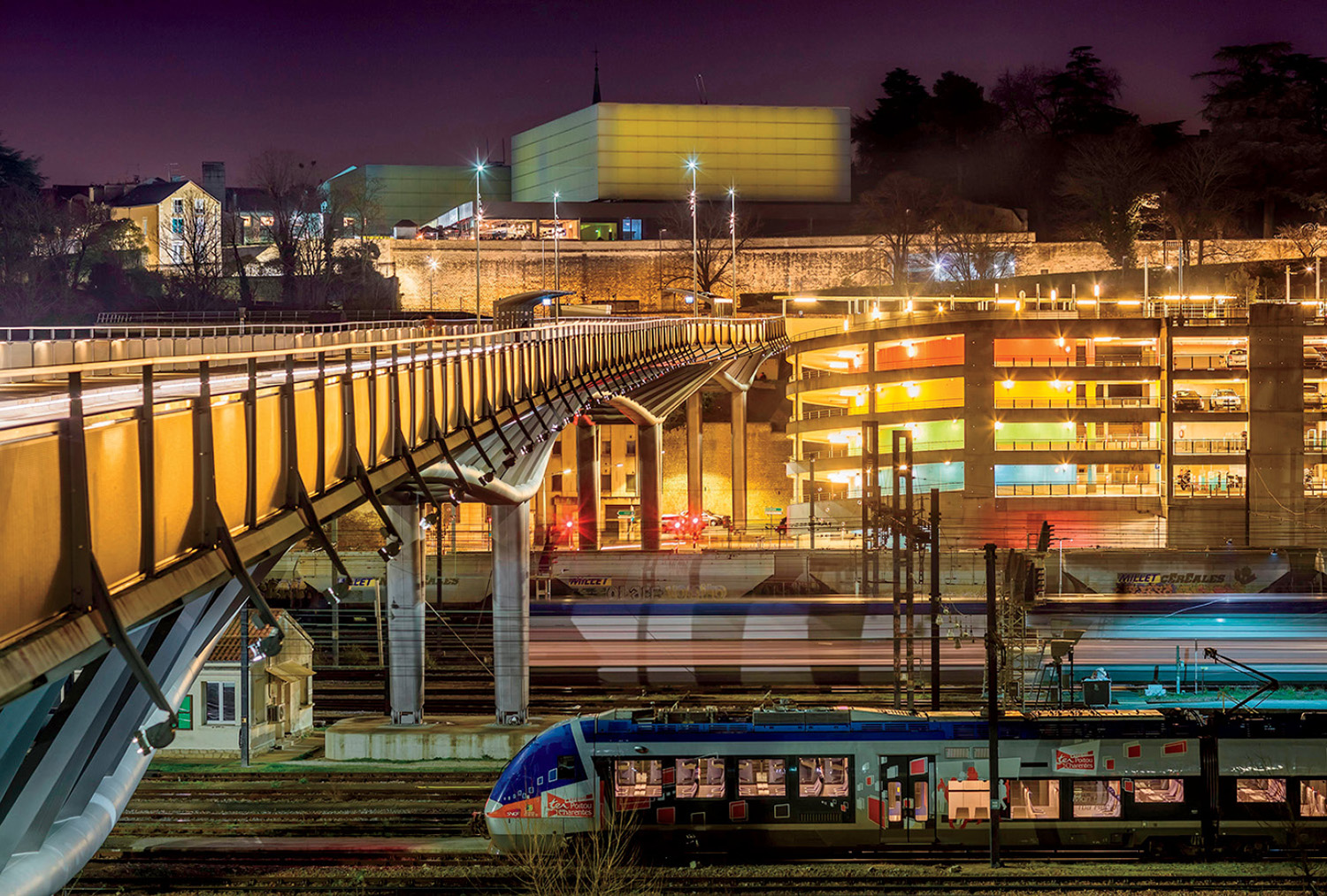 a bridge lit up at night near a parking garage