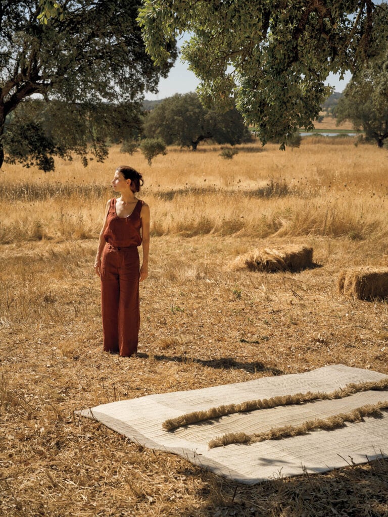 a woman in a field of wheat near a cream rug