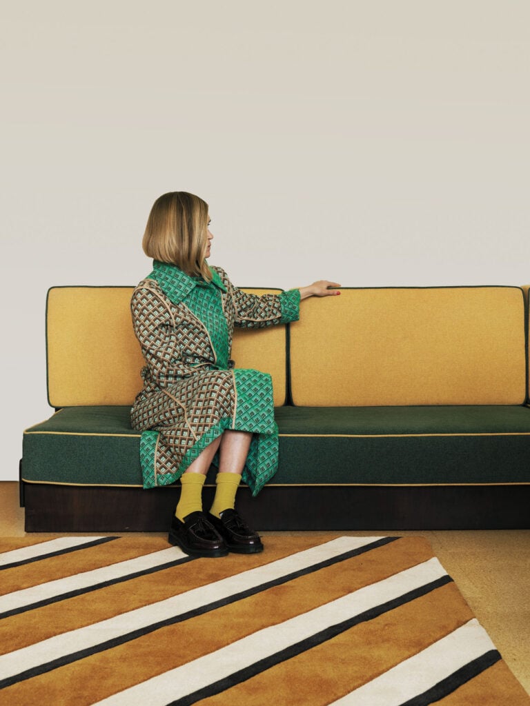 woman in green on yellow sofa atop brown and white striped rug